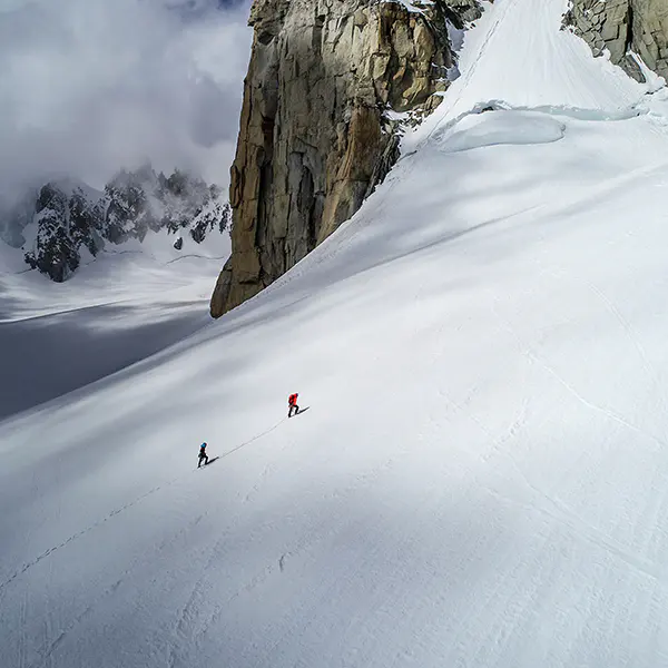 Twee bergbeklimmers die een steile, met sneeuw bedekte gletsjer beklimmen onder een rotsachtige klif. Twee bergbeklimmers die een steile, met sneeuw bedekte gletsjer beklimmen onder een rotsachtige klif.